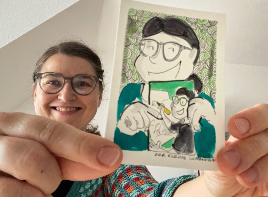 Katrin und der kleine Wahnsinn, Katrin hält ein Bild vom kleinen Wahnsinn, der wiederum ein Bild hält, auf dem der kleine Wahnsinn zeichnet